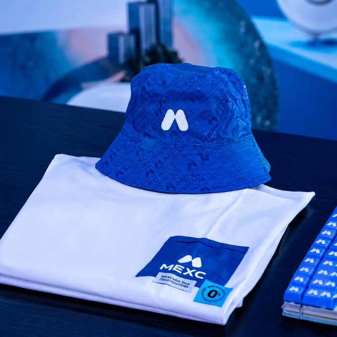 A blue MEXC Global bucket hat rests atop a folded white MEXC-branded t-shirt, accompanied by blue MEXC-branded accessories on the right. The image ties to the caption "I only trade wearing ___," with the obvious blank filled in by MEXC-branded merchandise, suggesting the trader exclusively wears MEXC apparel while trading.