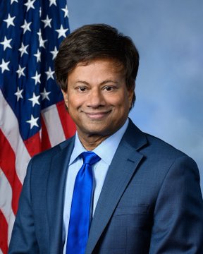 A formal portrait shows a smiling man with dark hair, wearing a blue suit and bright blue tie, posed in front of an American flag—the official style used for U.S. congressional photographs, matching the post's reference to Rep. Shri Thanedar. The image serves as a visual identification of the lawmaker criticized in the accompanying text for allegedly trading MicroStrategy stock while serving on the subcommittee shaping Bitcoin and digital asset policy.