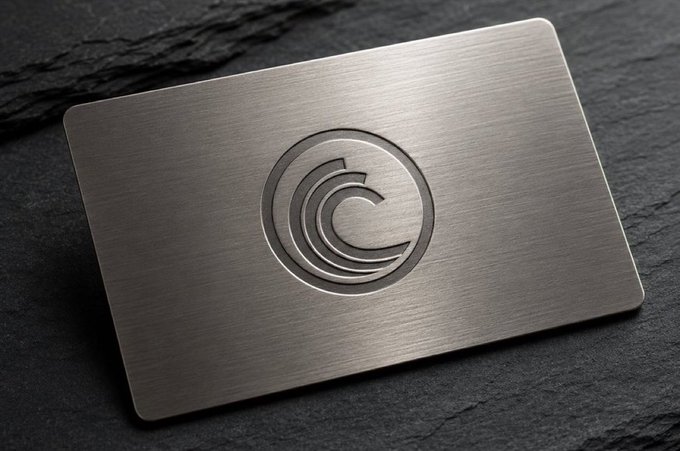 The image features a silver metal business card with an intriguing logo that resembles a wave. The wave symbol has a circle within it, which could represent a company's name or brand. The background of the image is black, providing contrast to the metallic sheen of the business card and making it stand out. The text on the card reads "The strongest networks are rarely the ones managed from the top", emphasizing the importance of collaboration and teamwork in the world of technology. This message could be related to the post about Bitcoin or another network that relies on peer-to-peer transactions, as indicated by the caption provided.