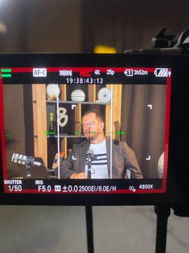 A camera monitor displays a man, identified as Nurkhat Kushimov, General Manager of Binance Kazakhstan, being filmed in a podcast studio setting, with on-screen settings showing "19:38:43:12," "F5.0," "ISO 2500," and "4800K." The viewfinder framing captures the behind-the-scenes filming process of the crypto podcast series in Kazakhstan.