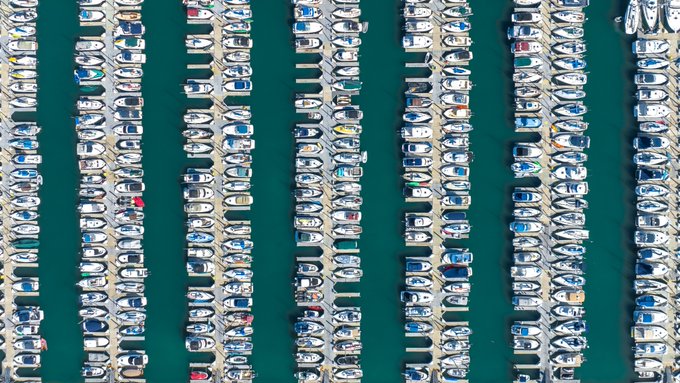 An aerial view of hundreds of boats tightly packed in neat rows within a marina, creating a striking repetitive pattern of white hulls against turquoise water. The image's geometric precision and overwhelming quantity evoke the "legion" theme referenced in the post.
