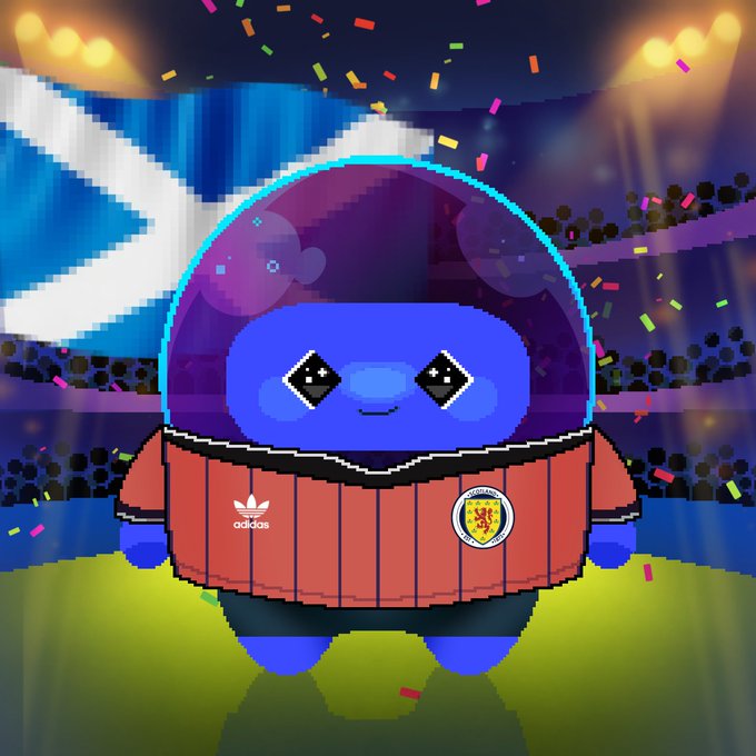 The image features a blue cartoon character wearing an orange shirt with a Scottish flag design on it. The character appears to be standing on a stage, possibly at a sports event or a celebration related to Scotland's national team. The caption of the image reads "Dlicom World Cup Collection #14 next stop: Scotland a nation famous for its kilts, bagpipes, and stunning Highland traditions which country should be next? @DlicomApp". This suggests that the character is likely representing Scotland in an event or celebration related to the Dlicom World Cup.