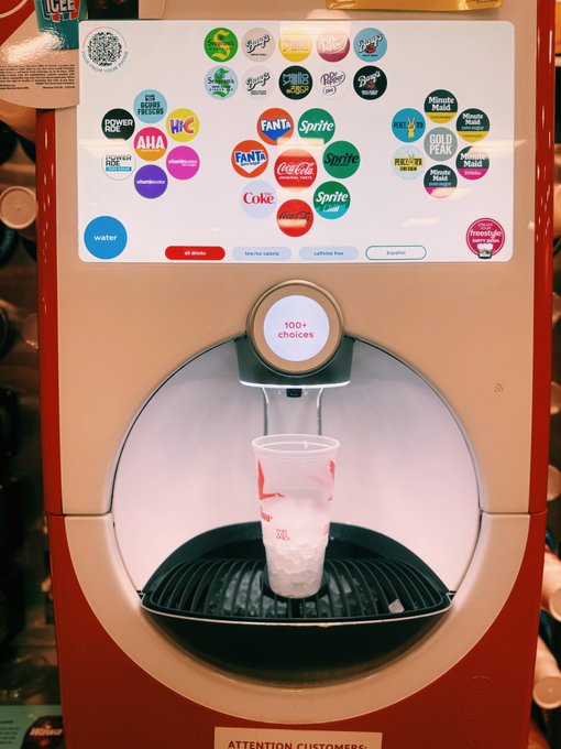 A Coca-Cola Freestyle machine touchscreen displaying various beverage brand logos (Fanta, Sprite, Coke, Minute Maid, etc.) with a cup of ice sitting in the dispensing area below.