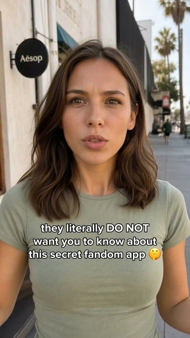 A woman with brown hair wearing an olive green t-shirt speaks to the camera on a street near an Aesop store; overlaid text reads 'they literally DO NOT want you to know about this secret fandom app' with a crying emoji.