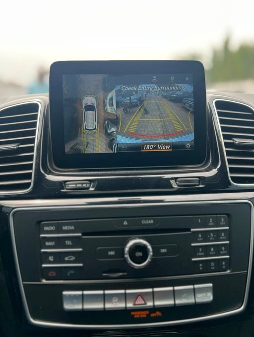 A car's infotainment screen displays a 360° 'Check Entire Surroundings' and '180° View' camera feed, showing other vehicles in a parking lot.