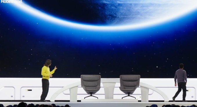 A Robinhood event stage with two presenters and two gray chairs on a white platform, set against a backdrop of a planet and starry sky.