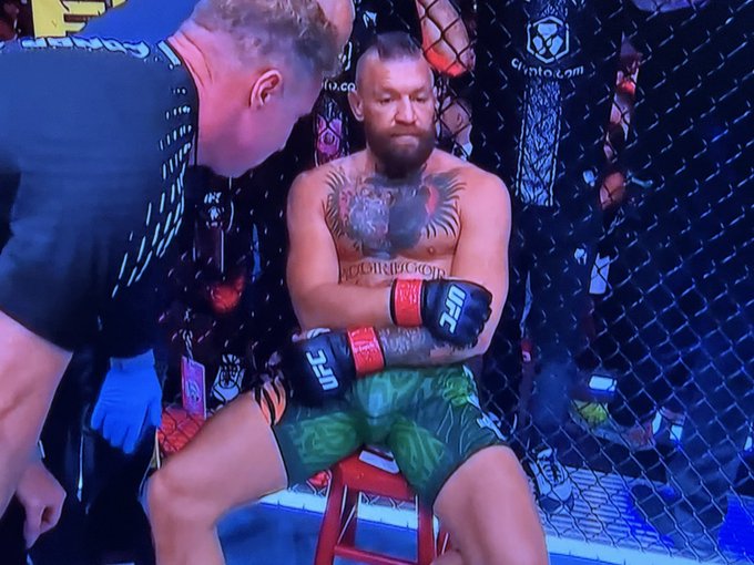 Conor McGregor sits dejectedly in the UFC octagon between rounds while a cornerman tends to him, with visible "crypto.com" and "UFC" branding on the cage and gloves. The image humorously portrays McGregor as defeated and grumpy, visually echoing the post's complaint about being told he's wrong on his $ETH (Ethereum) position.