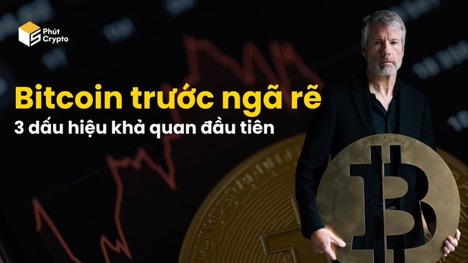 The image features a man in a black suit standing in front of a red Bitcoin price chart with a large gold Bitcoin coin, alongside the text "Bitcoin trước ngã rẽ - 3 dấu hiệu khả quan đầu tiên" (Bitcoin at a crossroads - 3 first positive signs) with the Phút Crypto logo in the top left, visually setting up the article's theme of analyzing Bitcoin market turning points despite recent large sell-offs.