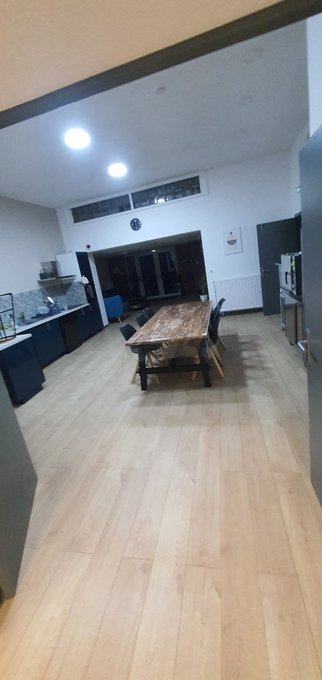 An interior view of a modern open-plan kitchen and dining area with a wooden table, bench, light-colored hardwood floors, and recessed lighting.