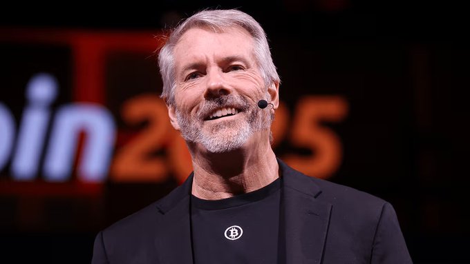 Portrait of Michael Saylor, Bitcoin advocate and MicroStrategy founder, wearing a Bitcoin pendant and speaking at a conference.