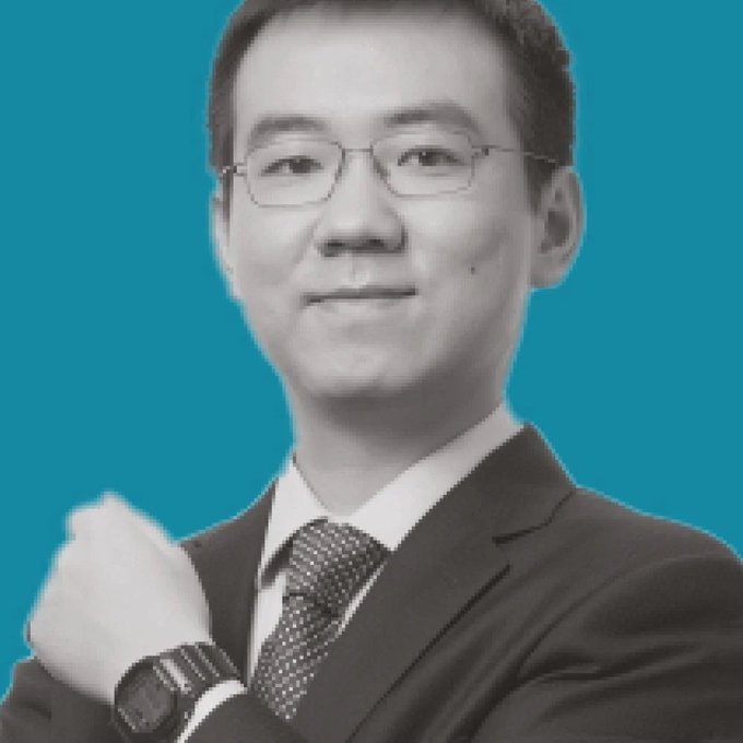 A black and white professional portrait of an East Asian man in a suit and tie with glasses, posed against a bright blue background.