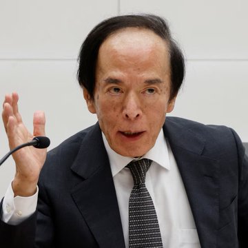 An elderly man in a dark suit and patterned tie gestures with his hand raised near a microphone, appearing to address an audience. The image likely depicts Bank of Japan Governor Kazuo Ueda announcing the historic 25 basis point interest rate hike, the highest Japan has seen in 31 years.
