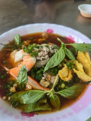 A bowl of Vietnamese soup, likely bún, garnished with fresh basil and herbs, served with shrimp on a floral-patterned plate.