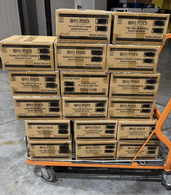 A cart stacked with 32 mixed One Piece TCG booster pack cases—including titles like "The Azure Sea's Seven," "The Time of Battle," "The World's Strongest Warriors," "Adventure on Grand Line," "Carrying On His Will," and "Awakening of the New Era"—delivered to the buyer, reflecting the post's note about a €100k+ shipment arriving in batches.