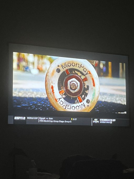 A TV screen displays a MoonPay commercial featuring a roulette-like wheel with "MoonPay" and "Moonward" text, airing on ESPN2 during coverage of the FIFA World Cup Group Stage match between Egypt and Iran. The image ties directly to the post, which celebrates spotting MoonPay's newly launched commercial as the first to tweet about it.