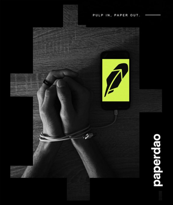 Two clasped hands bound by a charging cable sit beside a smartphone displaying a quill logo, with the text "PULP IN. PAPER OUT." above and the word "paperdao" running vertically along the right—visually echoing the post's call to commit $PULP to the Paper DAO treasury.