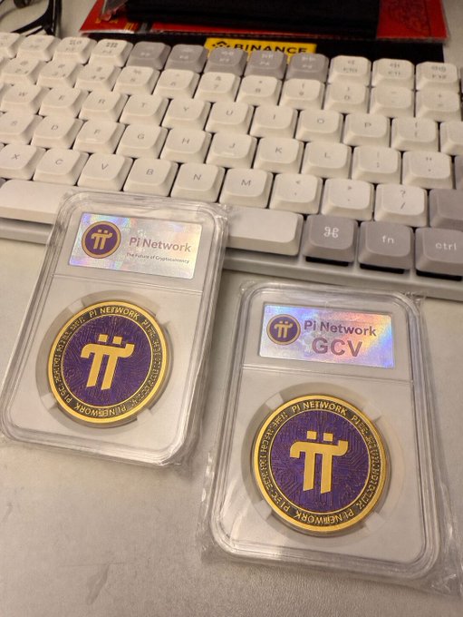 Two Pi Network commemorative coins in protective plastic cases rest on a white desk in front of a keyboard, with one labeled "The Pioneer Pi Network - The Future of Cryptocurrency" and the other marked "Pi Network GCV," referencing the post's praise of the GCV economic model and the community's strong consensus around the cryptocurrency.