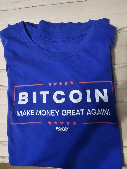 A folded blue t-shirt with a red-bordered design reading 'BITCOIN - MAKE MONEY GREAT AGAIN!' branded FOMC21.