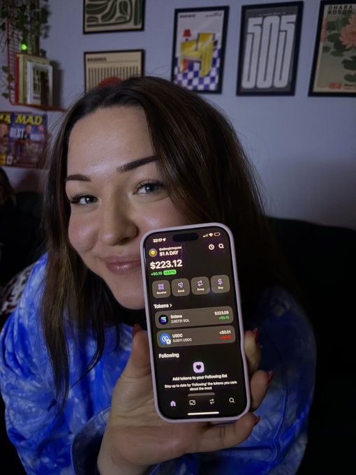 A woman smiles while holding up her phone displaying a Robinhood portfolio showing "$223.12" with "$1 A DAY" DCA plan, a small Solana (SOL) balance of "1.67 SOL" at "$223.00", and a "Following" section for an Instagram account — illustrating day 270 of her "$1 worth of SOL until ATH" investment challenge.