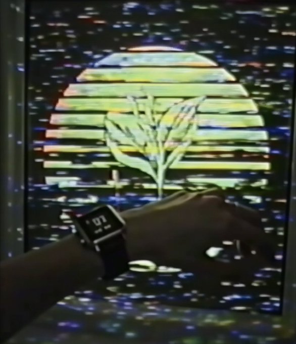 An arm wearing a Pebble smartwatch displays the time in front of a retro VHS-style graphic featuring a striped sunset and palm tree.