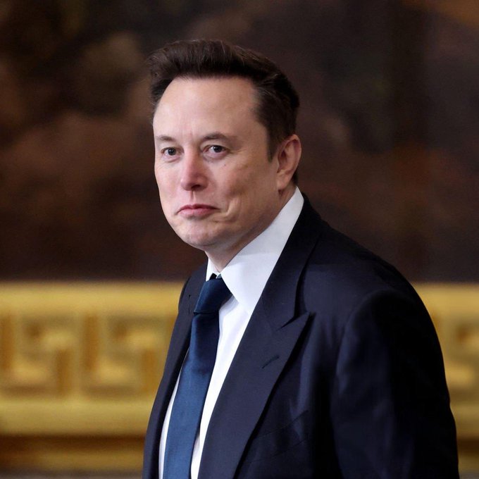 A man in a dark suit and blue tie stands with a serious expression in a formal setting with gold-trimmed decor. The image accompanies a post about Elon Musk reportedly attending Trump's state dinner for Xi Jinping, suggesting bullish implications for Tesla ($TSLA) in China amid this high-level diplomatic engagement.