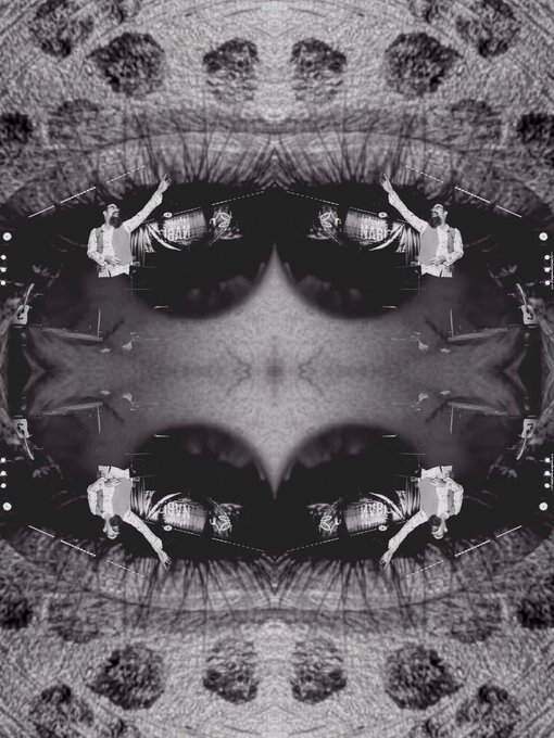A black-and-white mirrored kaleidoscopic image featuring symmetrical patterns with figures, including what appears to be a person in white, set against a dark, ornate backdrop.