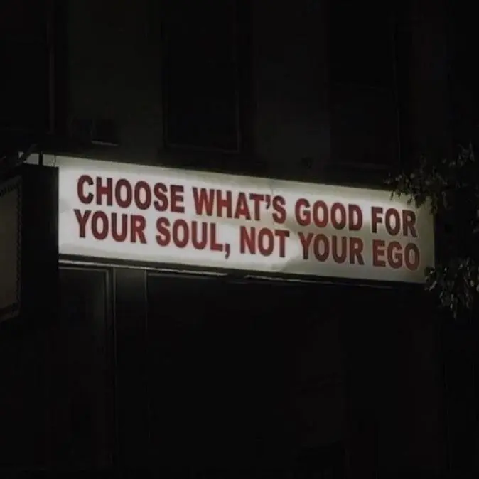 An illuminated sign at night reads 'CHOOSE WHAT'S GOOD FOR YOUR SOUL, NOT YOUR EGO' in bold red letters.