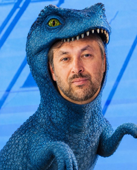 A man wearing a blue dinosaur costume with the head flipped back over his shoulders, posing against a light blue background.