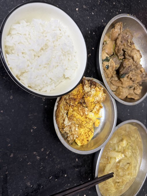 A dark countertop displays a simple daily meal: a white bowl of steamed rice alongside three small metal dishes containing stir-fried meat with greens, a fried egg omelet, and a creamy yellow curry-like dish, with chopsticks resting on the last bowl. The post humorously frames this humble rice bowl routine as a "stinky crypto-trading" meal, noting the swap of braised pork for two fresh eggs from home hens, while celebrating the first tokenized ETF stock listing on Backpack via the Solana contract address DRAMjSWR7HRfJKjRkvQWYL2bcaejaVhuxEcjf4pAY4Cw.