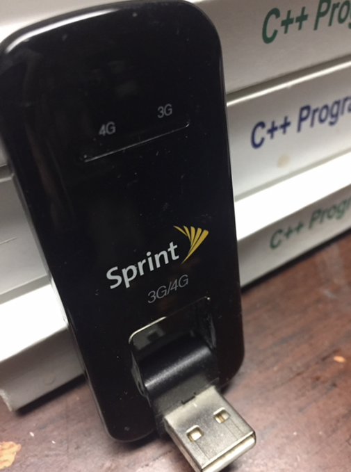 A photograph of a black Sprint 3G/4G USB modem/dongle plugged in, sitting in front of a stack of books labeled 'C++ Programming'.