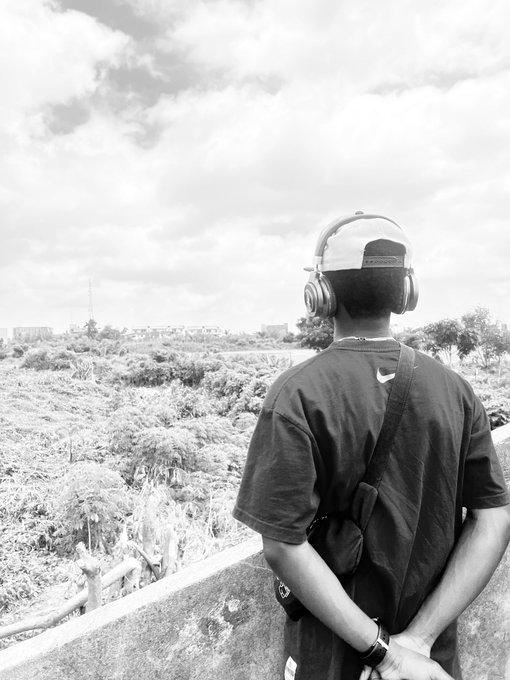 A young man wearing a backwards cap, headphones, and a crossbody bag stands overlooking a vast landscape, gazing into the distance as if waiting for his Bitget Wallet package to arrive.