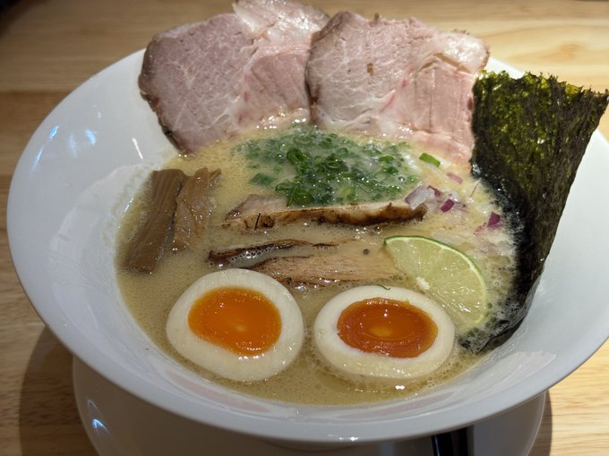 A bowl of rich tonkotsu ramen topped with chashu pork, marinated soft-boiled eggs, nori, and a lime wedge, serving as a hearty pre-run energy meal as the poster gears up for a run.