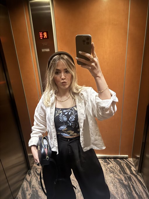 A young woman takes a mirror selfie in an elevator while holding her phone, with the display showing "19." Her relaxed weekend outfit and casual pose reflect the leisurely "Happy Weekend" vibe of the post, while the phone in hand subtly ties into the message about protecting digital data and privacy.