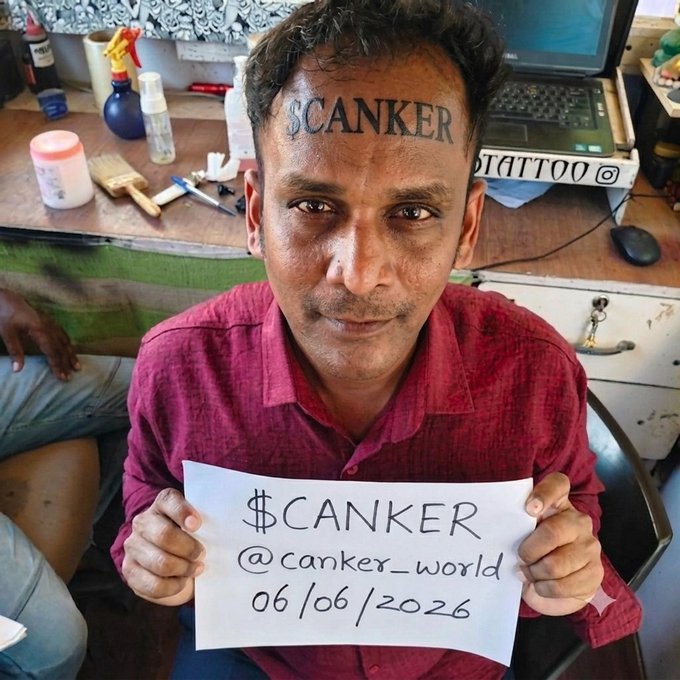 The image shows a man holding up a paper sign that says "Canker" with his fist, presumably indicating support for a crypto challenge involving tattoos. The man also has a tattoo of "Canker" on his forehead. A person's face is visible behind him but not clearly identifiable in the photo.