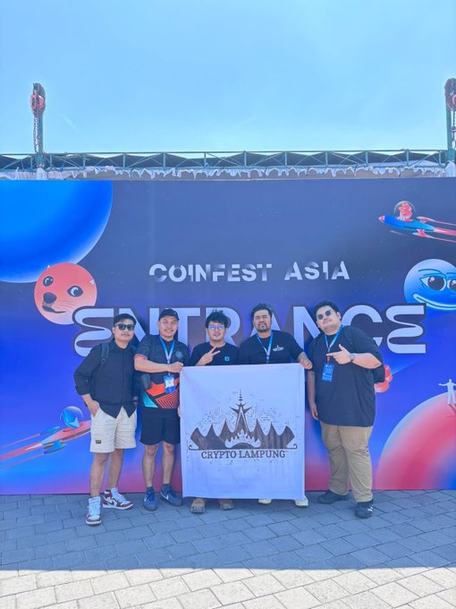 Five men pose in front of a blue "COINFEST ASIA" backdrop, with two holding a "CRYPTO LAMPUNG" banner featuring a mountain logo.