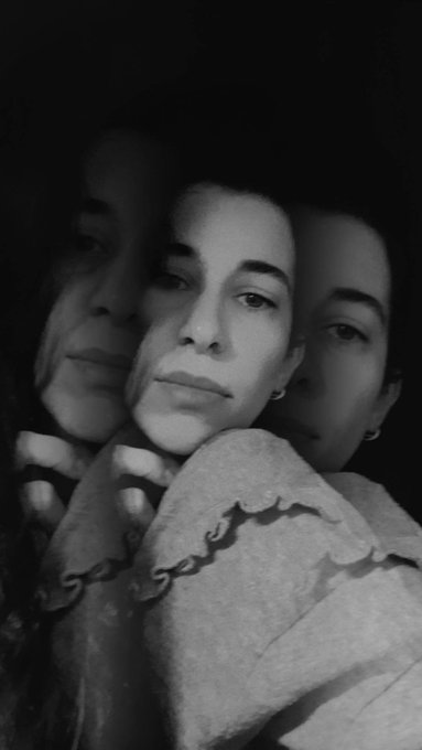 A black-and-white portrait featuring a double exposure effect, showing a woman's face repeated multiple times with a melancholic expression, wrapped in a textured shawl.