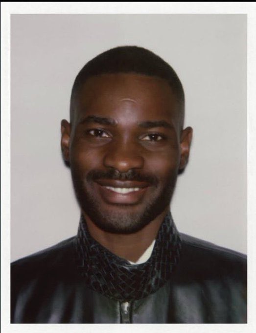 A portrait photograph of a smiling man wearing a dark patterned shirt, displayed in a vintage photo frame style.