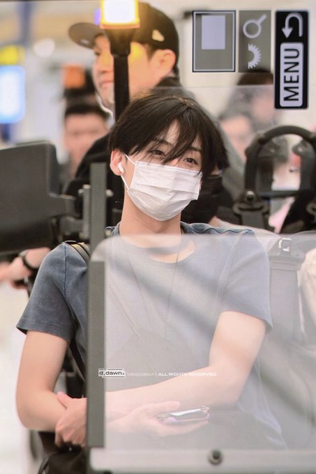 A young man with dark hair, wearing a white face mask and a gray t-shirt, is seated looking forward, appearing to be at an airport. The image includes overlays such as "MENU," "d:dawn:," and the text "@MADPRVT ALL RIGHTS RESERVED," and is associated with hashtags "#상원 #SANGWON #알파드라이브원 #ALPHADRIVEONE #ALD1," suggesting it depicts SANGWON arriving at ALD1.