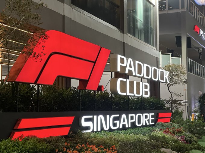 An illuminated sign for the Formula 1 Paddock Club Singapore, featuring the iconic red F1 logo with white text displayed in front of a modern building at night.