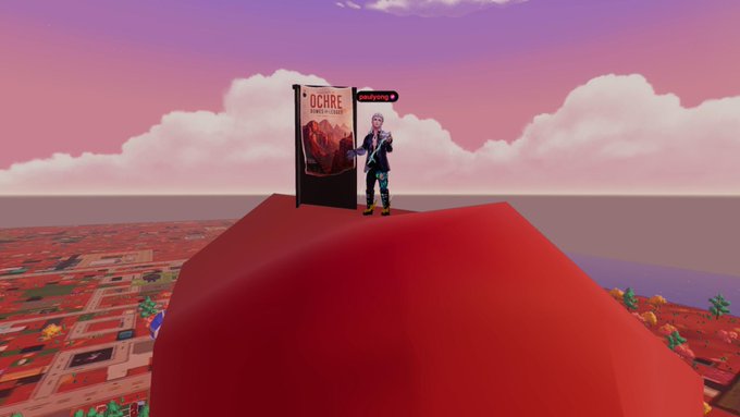 A low-poly 3D virtual world (likely Decentraland or similar) showing an avatar in dark clothing standing on a red platform next to a 'D CARE' banner, with a pink sky, clouds, and a blocky landscape extending into the distance.