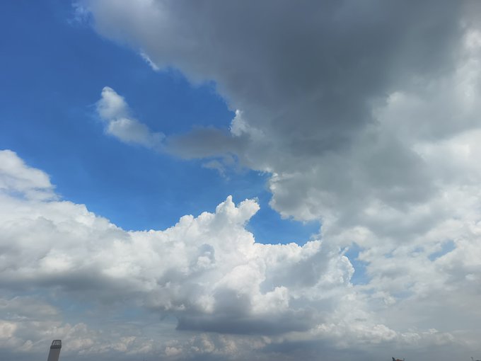 The image features a clear day with white clouds against a bright blue sky, suggesting an overcast mood or a possible change in weather. Below the cloud-filled sky, there's a person standing near some water under those same cloudy skies. The main focus of this photo is the contrast between the dark grey clouds and the lighter blue background. This striking image seems to have been captured during an activity on social media with a caption that reads "好多云啊 今天天气不错 继续交易 使用优势换取利润".