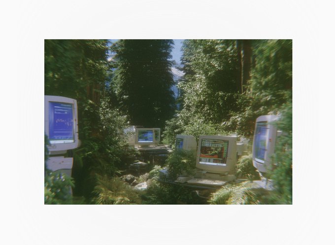 Old computer monitors displaying various screens are scattered throughout a lush, overgrown forest setting, reflecting the post's context of an NFT auction with a top bid of $70 by @lifeofc and only ~3 hours remaining.