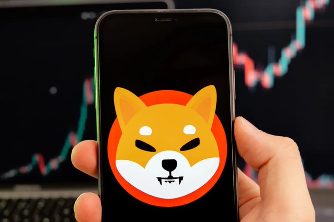 A hand holds a smartphone displaying the Shiba Inu (SHIB) logo, with a cryptocurrency price chart showing an upward trend visible in the background, visually reinforcing the post's message about SHIB's exchange reserves nearing 86.1 trillion tokens and tightening on-chain supply despite the token's downtrend at $0.0000041.