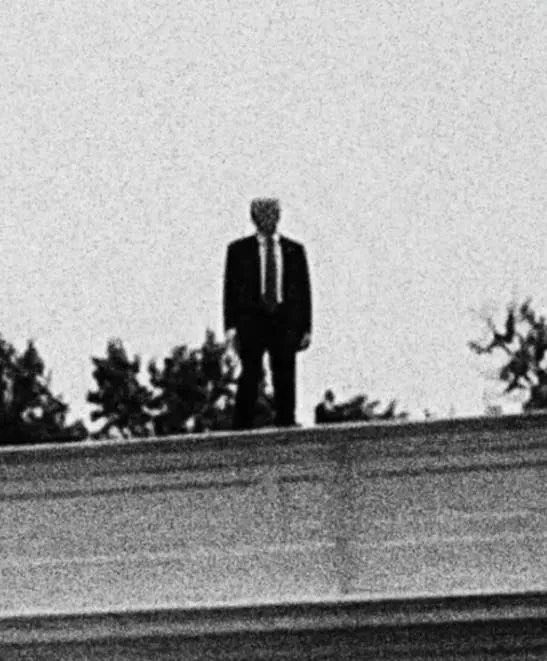 A grainy black-and-white image shows a distant figure in a dark suit standing silhouetted against a bright sky on what appears to be a rooftop or elevated ledge, with treetops visible in the background. The eerie, liminal figure evokes a sense of mystery or unease, fitting the post's tone of distancing from hype-driven crypto speculation and ending on a surreal "goodnight" note—as if the suited figure is silently watching over the chaos of meme coin rumors.