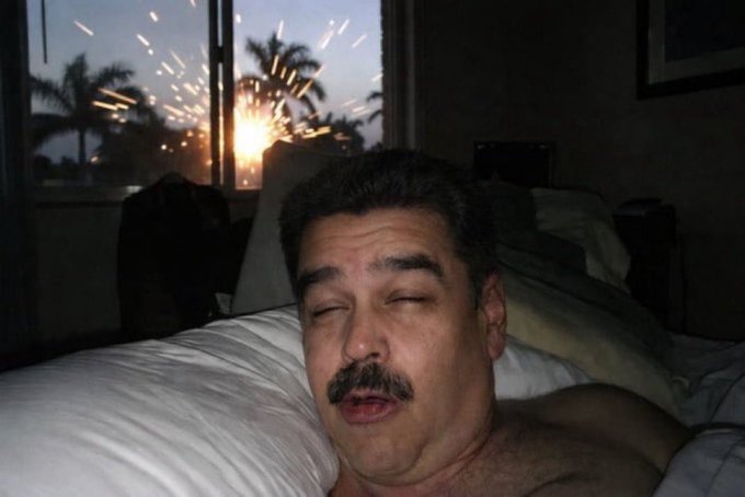 The image features a man lying down in bed with his eyes closed, possibly sleeping or resting. The scene takes place next to a window that has fireworks going off outside, creating an interesting contrast between the peacefulness of the man's restful moment and the excitement happening beyond the window.