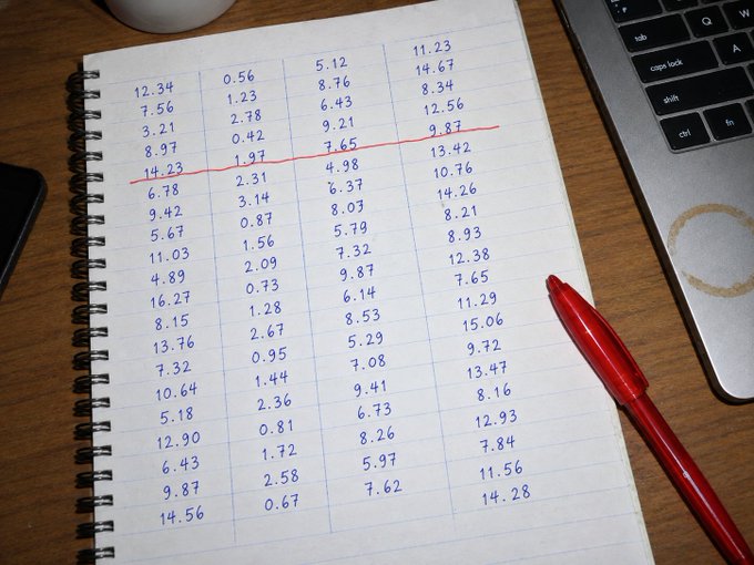 A spiral-bound notebook on a wooden desk filled with handwritten columns of numbers (decimals), with a red pen and a laptop keyboard (showing tab, caps lock, shift, ctrl, fn keys) visible nearby.