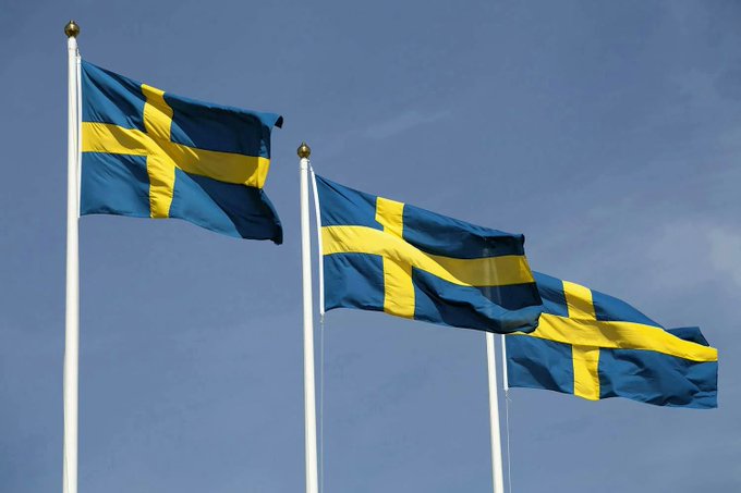 Three Swedish flags fly against a clear blue sky, symbolizing Sweden's role as the origin of B Treasury Capital AB, the pioneering European investment firm set to make history by distributing a 10% annual Bitcoin dividend yield to its shareholders.