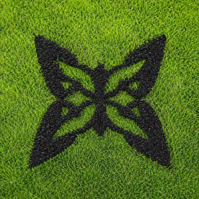 A black butterfly-shaped logo made of what appears to be rubber crumbs, laid out on a patch of bright green artificial grass.