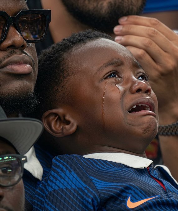 A young boy in a blue Nike jersey cries with tears streaming down his face while being held by a man wearing sunglasses, capturing the raw disappointment of a sports fan—visually echoing the post's theme of despair and loss among those not benefiting from early payouts.