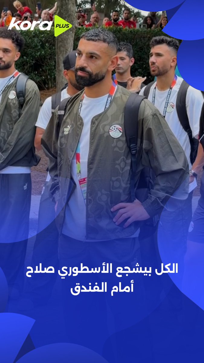 The image shows Mohamed Salah (featured centrally) and other Egyptian national team players wearing Puma jackets and lanyards, walking past fans gathered at a hotel. The Kora Plus logo is visible in the top-left corner, and Arabic text at the bottom reads "الكل يشجع الأسطوري صلاح أمام الفندق" (Everyone cheers for the legendary Salah in front of the hotel), matching the post's theme of fans supporting the Egyptian team and Salah.